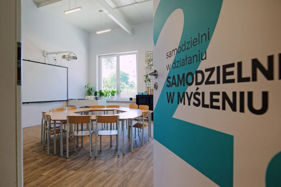 Sala lekcyjna ze wspólnym stołem, na drzwiach napis Samodzielni w myśleniu